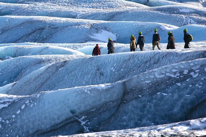 A small group hikes together on a glacier, exploring the dramatic icy landscape.
