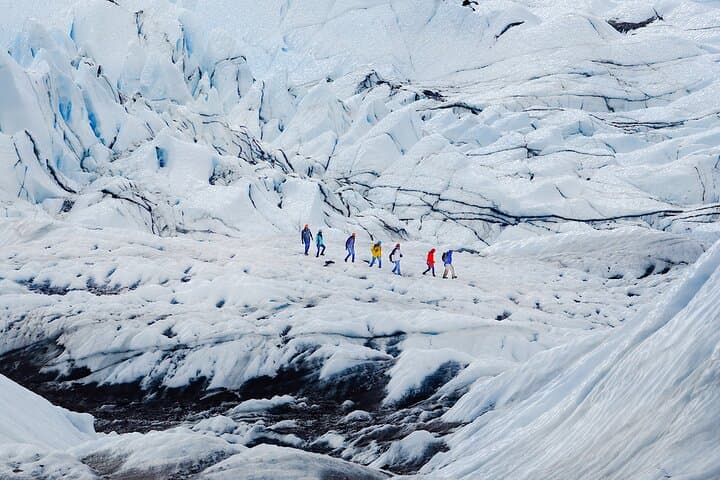 A group of adventurers makes their way across the vast Vatnajokull Glacier, surrounded by rugged ice formations.