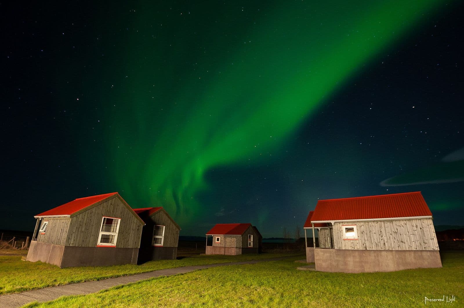 Green aurora over red-roofed cabins under a starry Icelandic sky