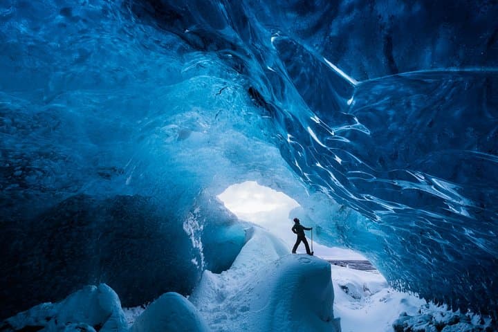 A visitor walks through icy blue tunnels while exploring an ice cave in Iceland.