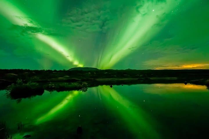 Emerald waves of the Northern Lights dance across the night sky, mirrored perfectly in the still waters below—a breathtaking harmony of light, color, and reflection in nature’s grand display.
