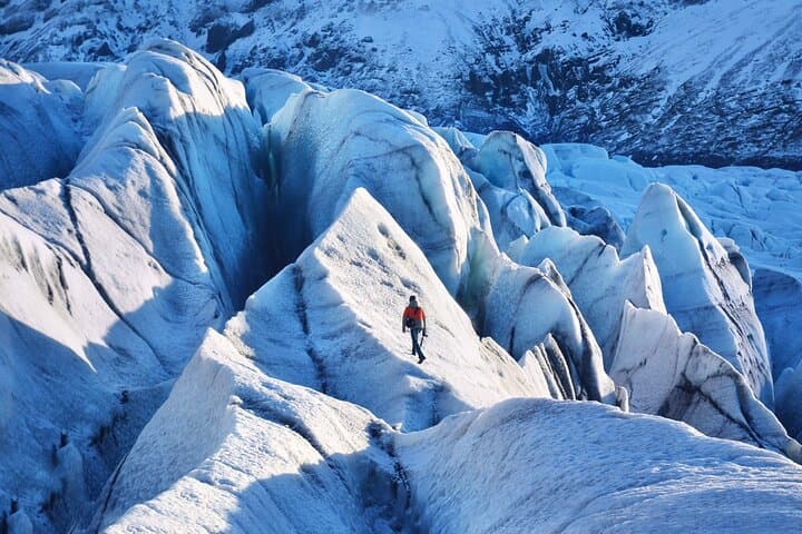 A person stands on a glacier with a rough, cracked ice surface stretching around them.