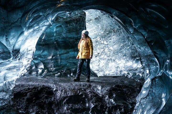 A woman walks through an ice cave and pauses to admire the frozen shapes.